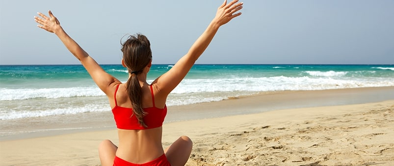 woman sitting on beach facing away from the camera with her arms in the air